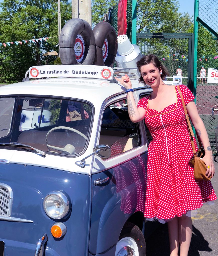Femme en robe rouge à pois blanc près voiture vintage